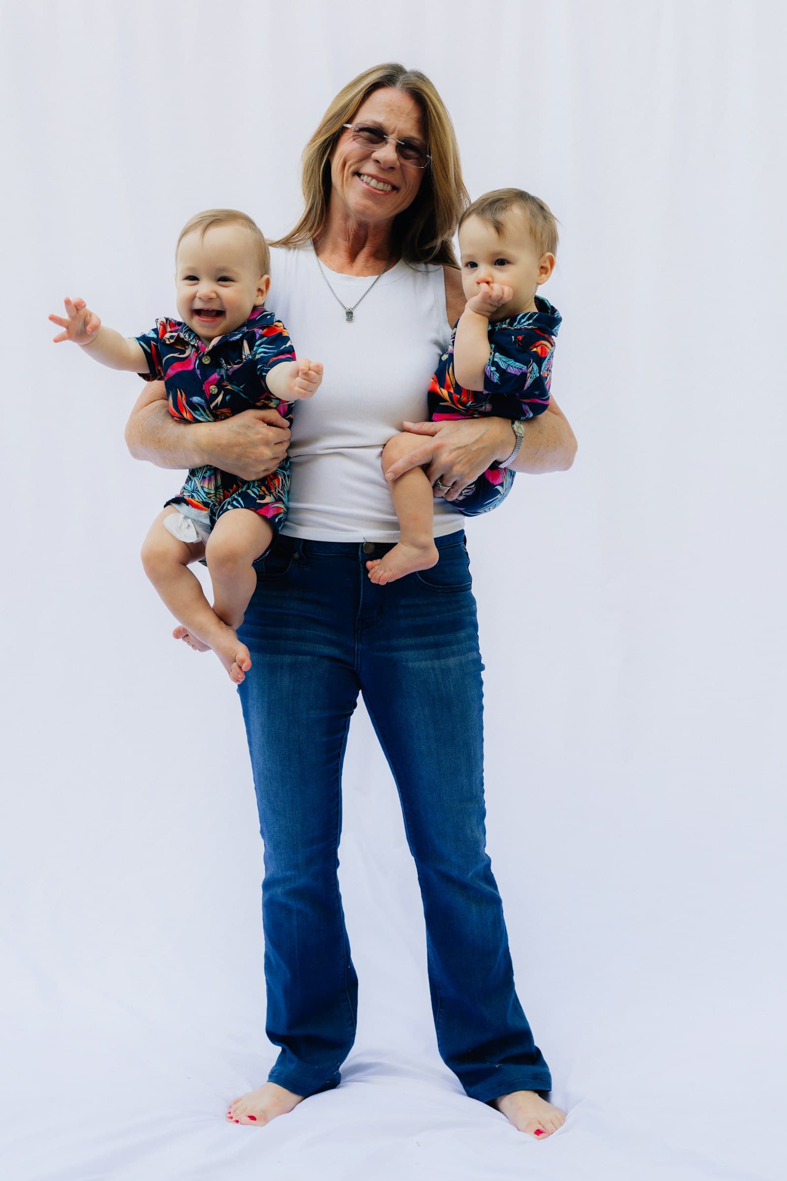 A parent holding two smiling twin babies in matching shirts
